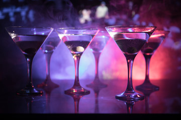 Several glasses of famous cocktail Martini, shot at a bar with dark toned foggy background and disco lights. Club drink concept