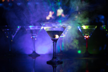 Several glasses of famous cocktail Martini, shot at a bar with dark toned foggy background and disco lights. Club drink concept