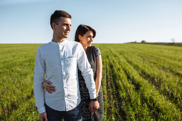 a young, happy, loving couple, standing in a green field, against the sky by the hands , and enjoy each other, advertising, and inserting text