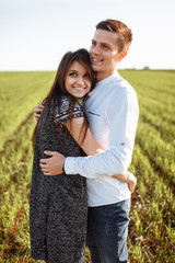 a young, happy, loving couple, standing in a green field, against the sky by the hands , and enjoy each other, advertising, and inserting text