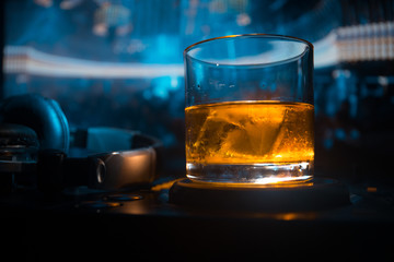 Glass with whisky with ice cube inside on dj controller at nightclub. Dj Console with club drink at music party in nightclub with disco lights.