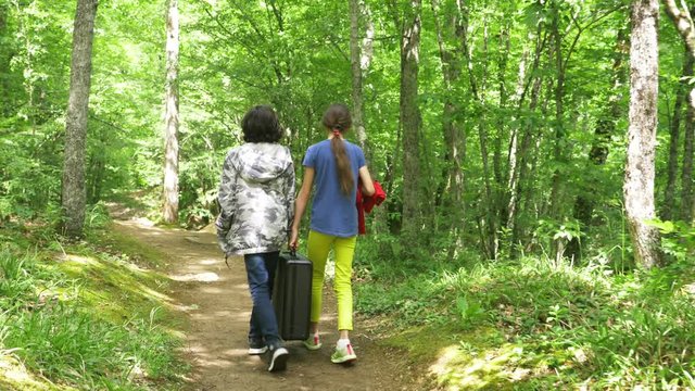 girl and boy, walks through the woods with a heavy black suitcase. 4k, slow-motion shooting, steadicam shot.