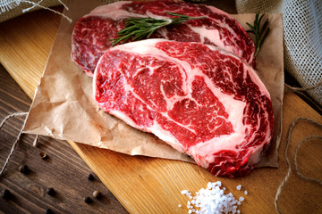 Two raw rib eye steak on a wooden Board on a table prepared for the grill. Top view rustic style