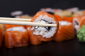 Mens hand holding wooden sticks Philadelphia roll with salmon on black background