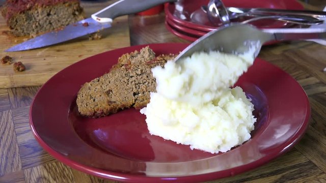 Spooning hot steaming mashed potatoes onto a plate

