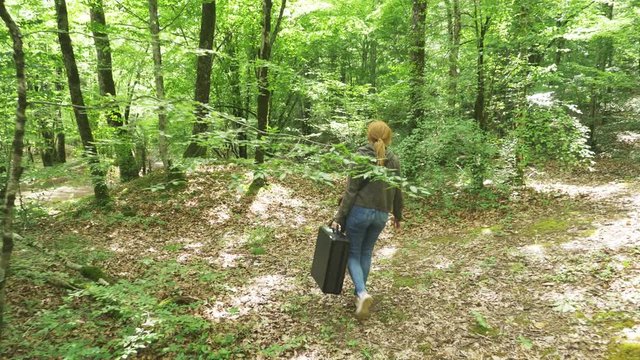 girl, walks through the woods with a heavy black suitcase. 4k, slow-motion shooting, steadicam shot.
