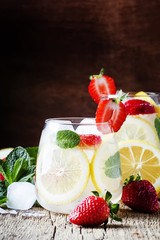 Non-alcoholic cocktail with strawberries, mint, lemon, soda and ice, old wooden background, selective focus