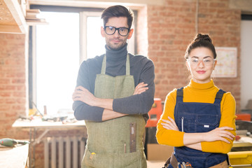 Fototapeta premium Waist up portrait of young female artisan posing in crafting shop standing with arms crossed and looking at camera next to colleague, copy space