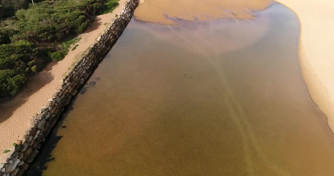 Shallow sandy lagoon of Narrabeen Lake at the entrance to Pacific ocean and sandy beach with rock pool near sandstone headland. 
