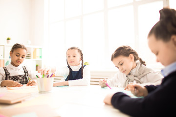 Schoolchildren drawing with highlighters at lesson together at the desk