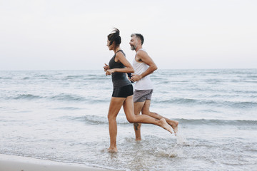 Couple jogging on a beach - obrazy, fototapety, plakaty