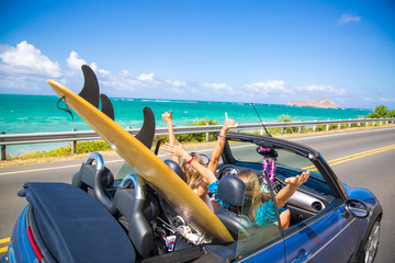 Road trip travel - girls driving car in freedom. Happy young girls cheering in convertible car on summer Hawaii vacations. - obrazy, fototapety, plakaty