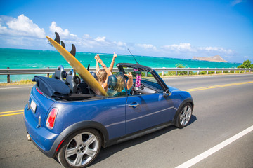 Road trip travel - girls driving car in freedom. Happy young girls cheering in convertible car on summer Hawaii vacations. - obrazy, fototapety, plakaty