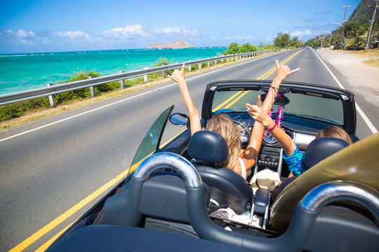 Road trip travel - girls driving car in freedom. Happy young girls cheering in convertible car on summer Hawaii vacations.