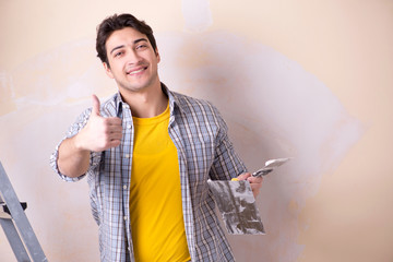 Young man applying plaster on wall at home