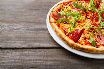 Hot appetizing Italian pizza with prosciutto and arugula, delicious food close up with copy space. Pizza delivery, restaurant, menu, recipe, pizzeria concept