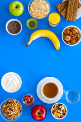 Make a menu for wholesome breakfast. Fruits, oatmeal, yogurt, nuts, crispbreads, chia on blue background top view copy space