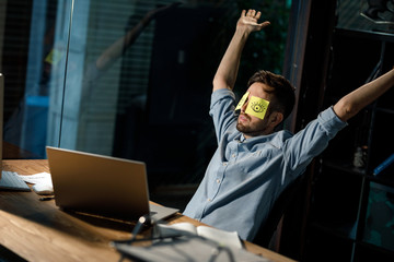 Man sitting at laptop in office with sticky notes with eyes on face. 