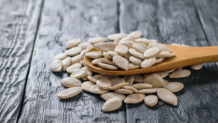 A spoon with pumpkin seeds on a dark rustic table.