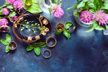 Golden bracelets and rings in a feminine style concept with clover flowers on a dark background. Beautiful summer accessories.