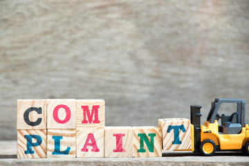 Toy forklift hold letter block T to complete word complaint on wood background