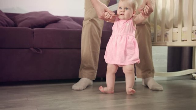 Beautiful baby girl stand up with father support. Infant learning walk. Child learning walk with daddy. First step in life. Sweet childhood. Happy family love. Parent care baby