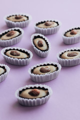 Flat lay of delicious praline sweets with almonds on purple background