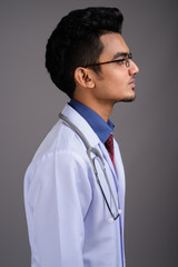 Young Indian man doctor against gray background