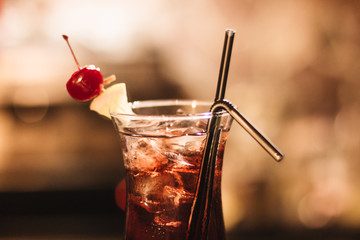 Delicious cocktail with ice cubes, cherry and straws in bar