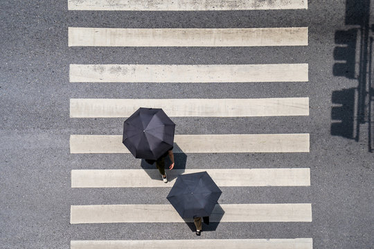 Aerial photo top view of people under umbrella walk on street in the city over pedestrian crossing traffic road