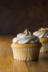 Cup cakes with white frosting on wooden table, focus on front cupcake