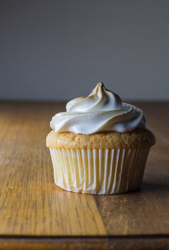 Single cup cake with white topping on wooden table close up