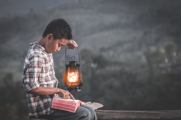 Boy holding oil lamp and reading bible, christian concept