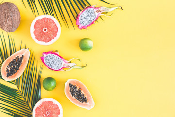 Summer fruits. Tropical palm leaves, pineapple, coconut, papaya, dragon fruit, orange on yellow background. Flat lay, top view, copy space