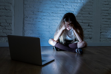 Sad young girl with laptop suffering bullying and harassment online. Cyberbullying, online gaming