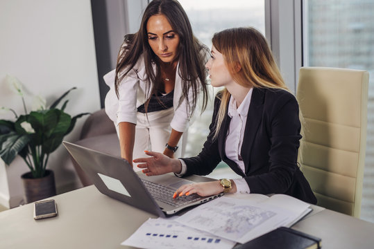 Young female assistant consulting with a top manager showing data on laptop screen and asking for advice sitting at working place