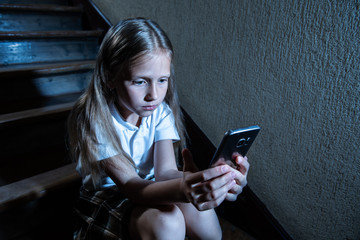 Sad depressed unhappy child suffering from cyberbullying by mobile smart phone sitting alone.