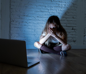 Sad young girl with laptop suffering bullying and harassment online. Cyberbullying, online gaming