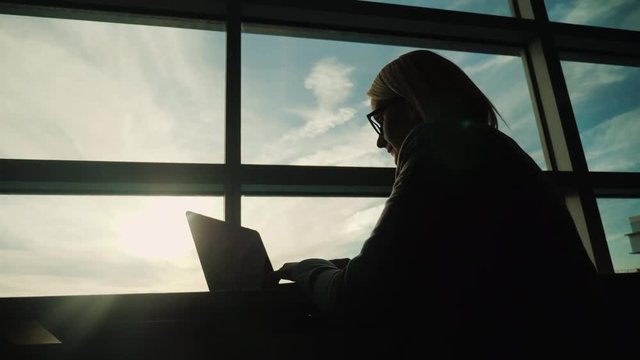 Woman in business suit working with laptop at large office window