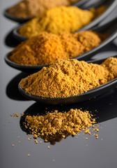 Small black bowls of Indian spices on black reflective background .