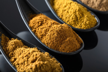 Small black bowls of Indian spices on black background .