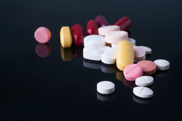 Medical pills with different size, shape and color on black glass table with reflection.Studio shot.