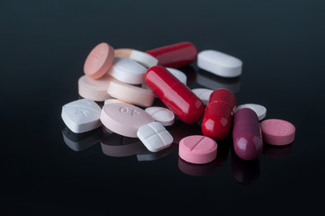 Medical pills with different size, shape and color on black glass table with reflection.Studio shot.