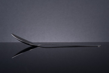 Steel spoon on black glass table with reflection.