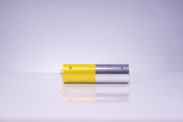 Yellow and silver alkaline AA battery isolated over white background with reflection.