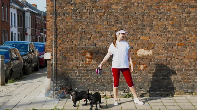 CINEMAGRAPH - SEAMLESS LOOP. Portrait of young Caucasian girl holding 2 black french bulldogs against brick wall