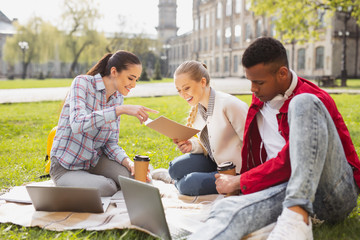 Busy undergraduates. Three busy undergraduates feeling overloaded while preparing their home assignment sitting on the grass together