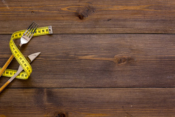 Proper nutrition for slimming. Fork and knife with wound measuring tape on dark wooden background...