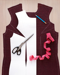 Sewing a dress using a paper pattern. Paper pattern of clothing on the fabric. Tailoring scissors, a centimeter tape and a drawing of the base of the dress are seen from above.