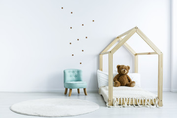Simple kid room interior with diy bed with a teddy bear, armchair, round rug and stars on the wall. Place for your product © Photographee.eu
